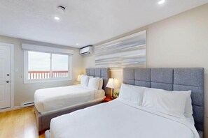 Ein Hotelzimmer mit zwei Betten, einem Fenster mit Blick, einer Wand-Klimaanlage und einem modernen Wandbild.