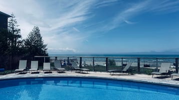 A pool with lounge chairs and a view of the ocean.