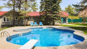 Una piscina con un jacuzzi, sillas de descanso y un pequeño edificio con techo rojo.