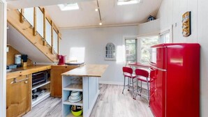 Una cocina con armarios de madera, un refrigerador rojo y una zona de comedor con sillas rojas.