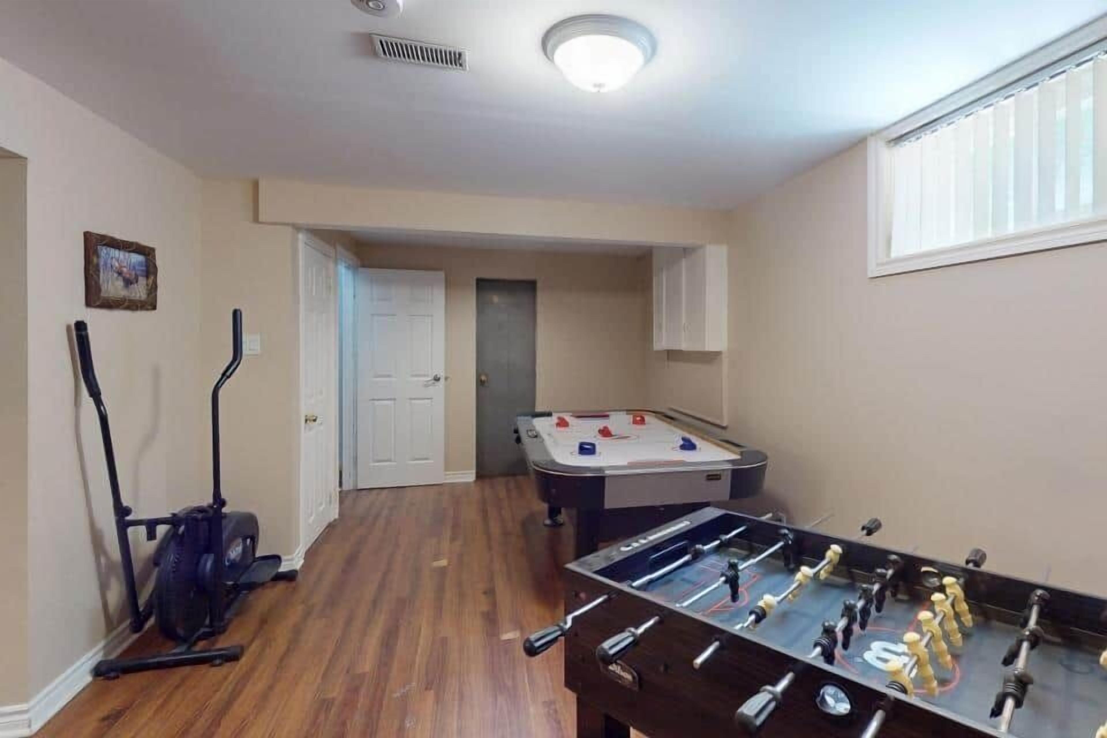A room with a foosball table, exercise equipment, and a door leading to another room.