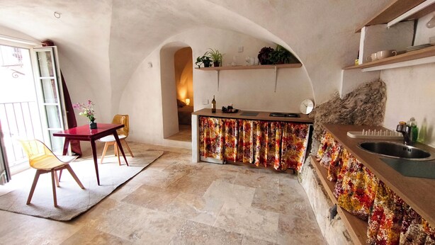 A compact kitchen with a central island, a dining area with chairs, and a view through an archway to a bedroom. - Atypical and central apartment in Fontaine de Vaucluse (Fontaine-de-Vaucluse)