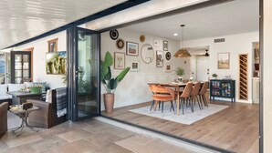A modern dining area with a glass door leading to a patio, a dining table with chairs, and a kitchen visible through the glass.