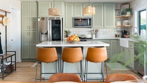 A kitchen with a central island, three bar stools, a refrigerator, a microwave, and a sink.