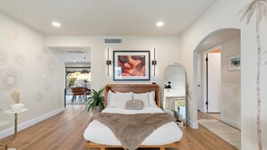 A bedroom with a bed, a framed picture above it, and a hallway leading to another room.