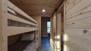 Un corridoio stretto in legno con letti a castello da un lato e una porta che dà su un'altra stanza.