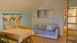 A room with a dining table, a sofa with cushions, a painting on the wall, and a ladder. - Studio on the road to the beaches Trégunc France (Trégunc)