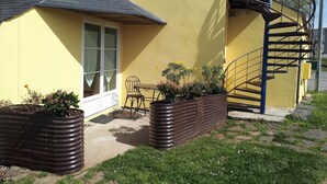 Een geel gebouw met een raam, een deur, een trap en een klein terras met een tafel en stoelen.