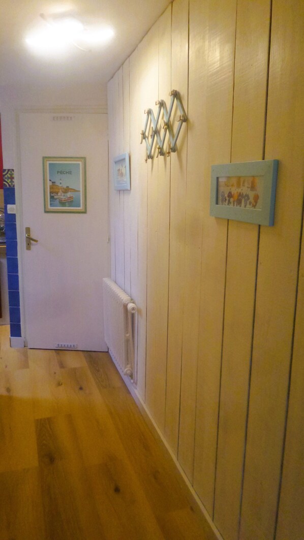A hallway with wooden paneling, a radiator, and framed pictures on the wall. - Studio on the road to the beaches Trégunc France (Trégunc)