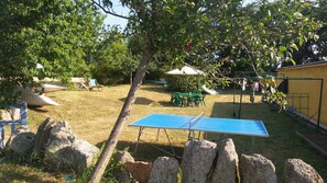 A backyard with a ping pong table, green chairs, a table with chairs, and a yellow building. - Studio on the road to the beaches Trégunc France (Trégunc)