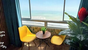 A room with a large window overlooking a beach, two yellow chairs, a small round table, and a potted plant. - Perfect 3-bedroom apartment in enchanting Callao for your stay (Callao)