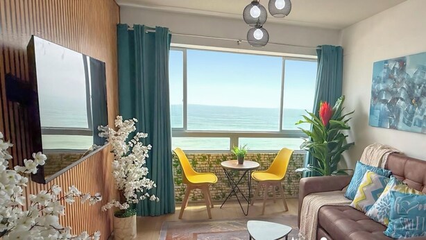 A living room with a view of the sea, a sofa, two yellow chairs, a TV, and a potted plant. - Perfect 3-bedroom apartment in enchanting Callao for your stay (Callao)