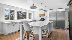 A modern kitchen with white cabinetry, a large island with bar stools, a stainless steel refrigerator, and pendant lighting. - Spacious family-friendly 5-bedroom house in Kalispell, MT (Kalispell)