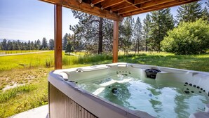 Een hottub onder een houten pergola, met een grasveld en bomen op de achtergrond.