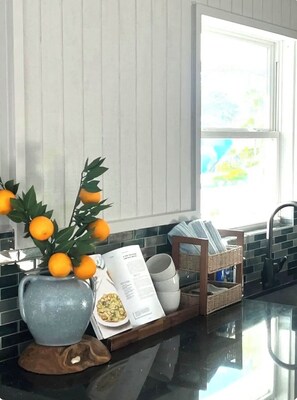 Eine Küche mit Fenster, einer Vase mit Orangen und einer Ablage mit Schüsseln und einem Buch.