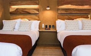 Habitación de hotel con dos camas, una mesita y una lámpara fijada a la pared.