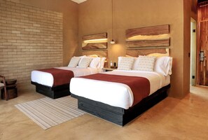 Cama doble con cabecera de madera y detalle rojo, mesita de noche y pared de ladrillo.