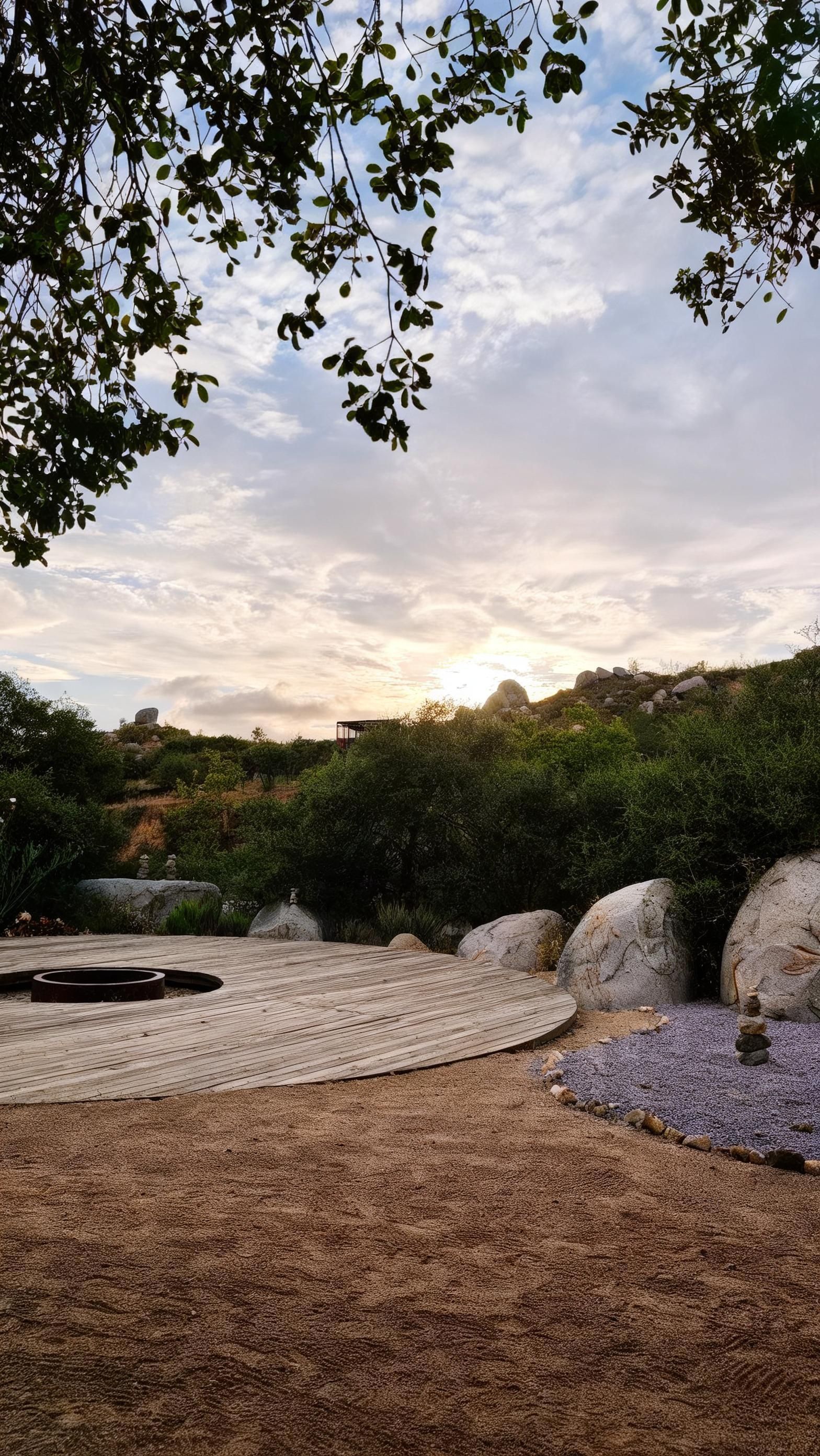 Une terrasse en bois dotée d’un foyer circulaire, entourée de gravier et de rochers.