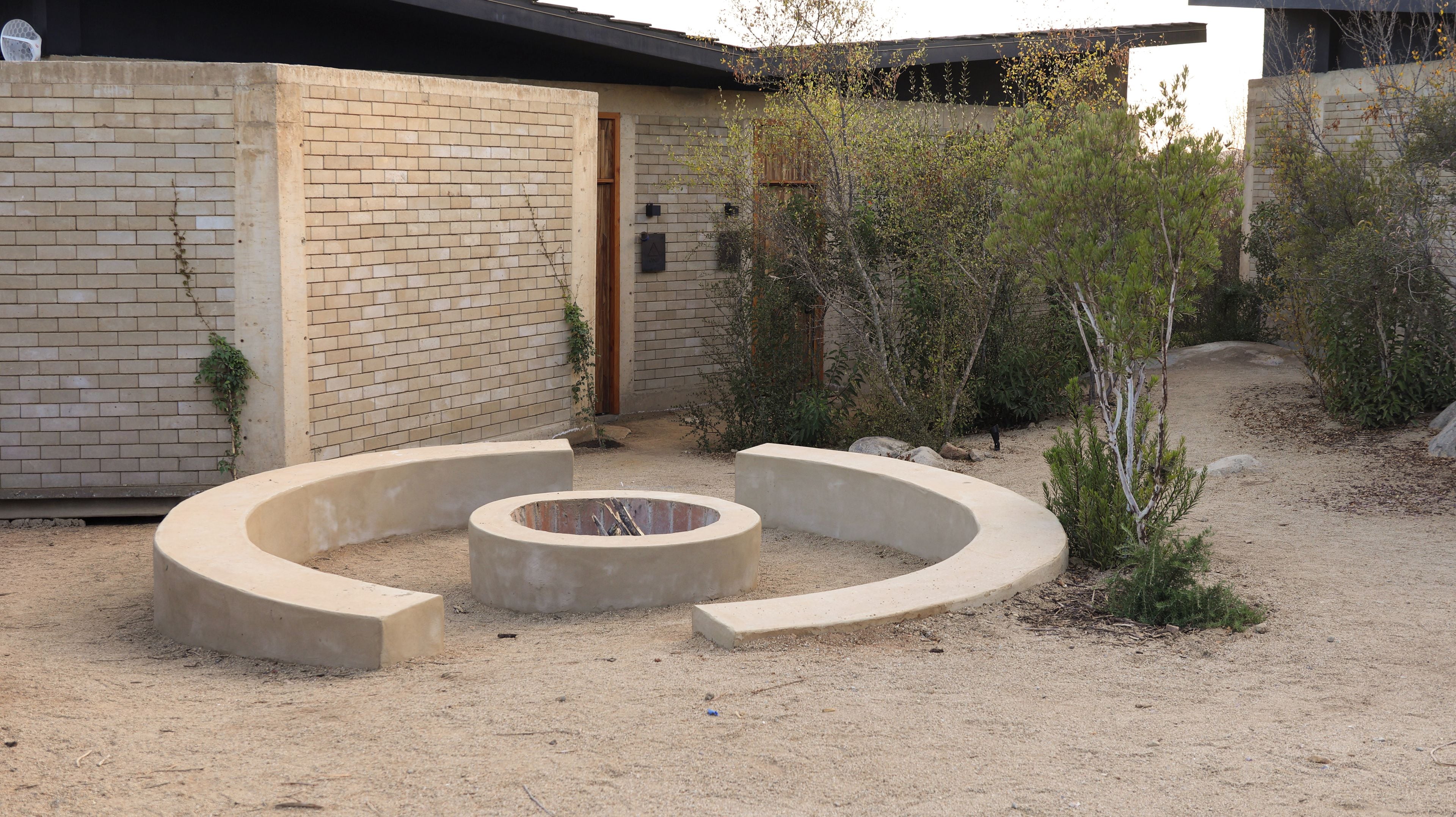 Une cour dotée d’un espace de repos circulaire en béton, d’un mur en briques et d’une végétation clairsemée.
