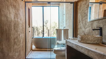 A modern bathroom with a glass door, a freestanding bathtub, a stone sink, and a large mirror.