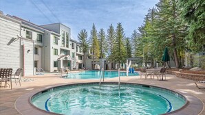 A pool area with a hot tub, lounge chairs, and a building with multiple windows. - VIP Palisades Condo A+ Location Views Hot-Tub (Olympic Valley)