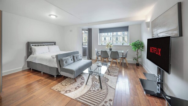 Una sala moderna con cama, sofá, televisión y zona de comedor.