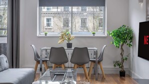 Una sala moderna con un sofá, una mesa de comedor con sillas, una planta en maceta y un televisor en la pared.