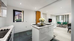 A modern kitchen with a built-in stove, a dining area with a green chair, and a TV displaying 'NETFLIX'. - Luxurious Three Bedroom With Balcony (London)