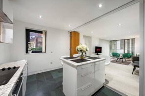 A modern kitchen with a built-in stove, a dining area with a green chair, and a TV displaying 'NETFLIX'. - Luxurious Three Bedroom With Balcony (London)