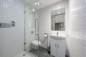 A modern bathroom with a glass shower enclosure, a white toilet, a sink with a mirror, and a tiled wall. - Luxurious Three Bedroom With Balcony (London)