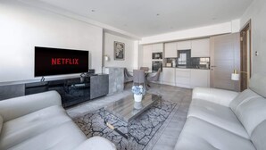 A modern living room with a flat-screen TV, a glass coffee table, and a sofa.