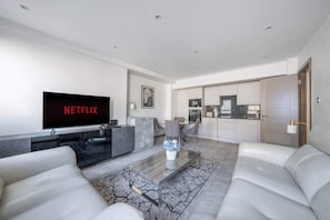 A modern living room with a flat-screen TV, a glass coffee table, and a sofa.