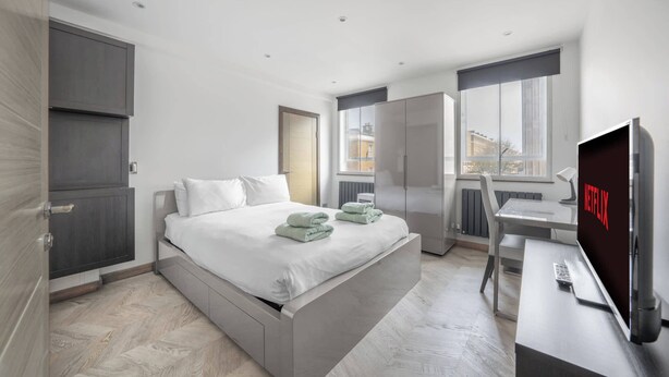A modern hotel room with a bed, wardrobe, desk, and TV.