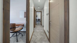 A hallway with a wooden door, a desk with a chair, and a tiled floor.