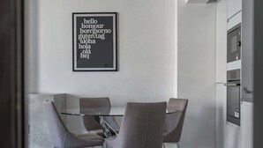 A modern kitchen with a glass table and four chairs, a framed text on the wall, and built-in appliances.