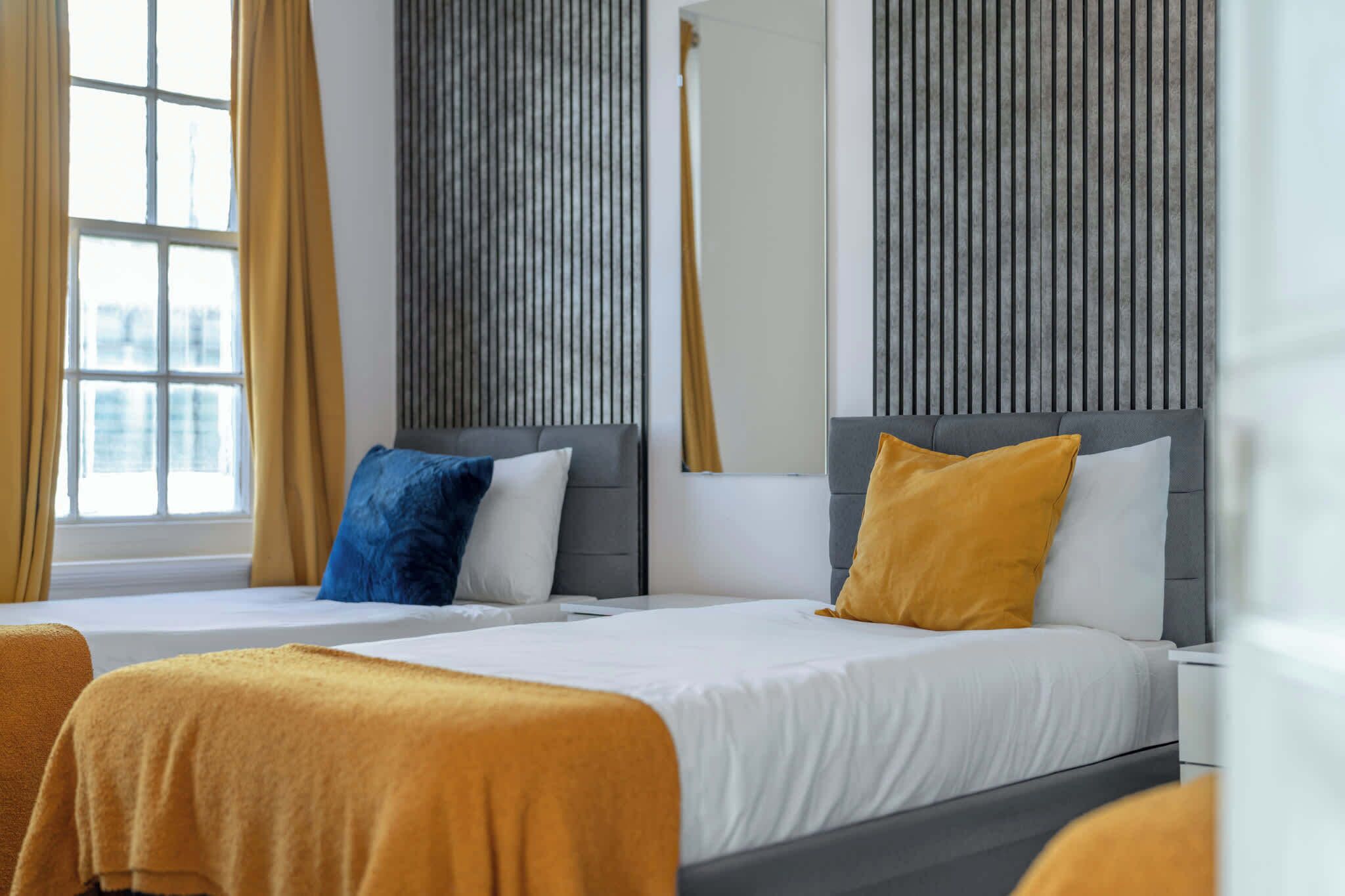 A hotel room with two beds, a large window, and a vertical wooden panel on the wall.