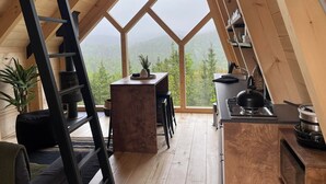 Une chambre confortable située dans les combles, avec une échelle en bois, un petit bureau et une vue sur la forêt.