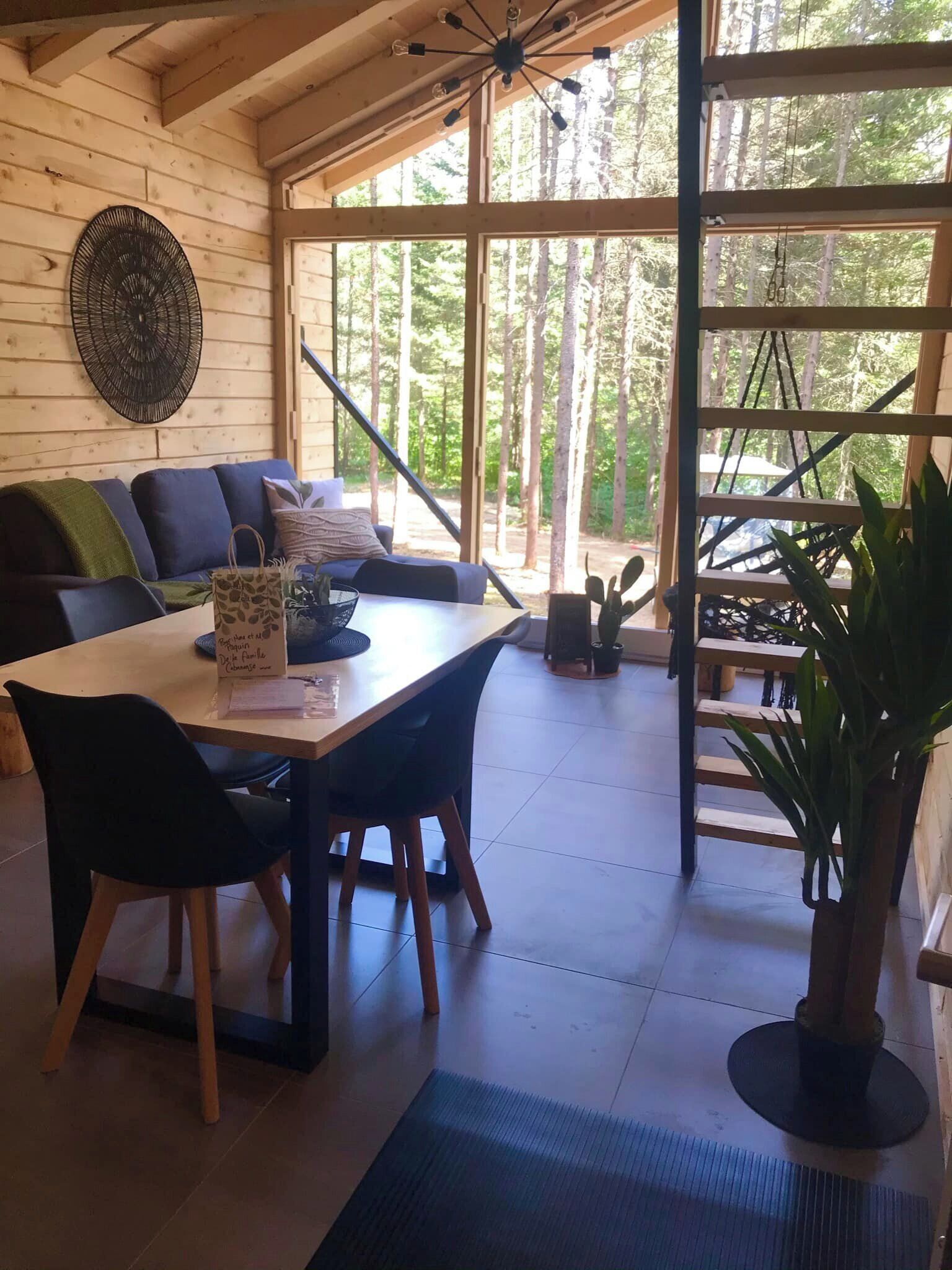 Un interior de madera con una mesa de comedor, sillas, un sofá y un ventanal con vistas a un bosque.