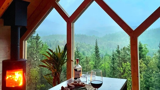 Une pièce dotée d’une grande fenêtre, d’une cheminée, d’une table avec de la nourriture et des verres à vin, et d’une bouteille.