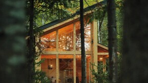 Une cabane dotée de grandes fenêtres, d’un revêtement extérieur en bois et d’un intérieur visible, comprenant un coin repas.