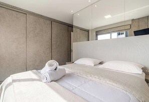 A modern hotel room with a large bed, a headboard, and a view of the outside through a window. - Luxury 2BR • 2 Min Walk to Beach • Rooftop Pool • BBQ • 2 Parking (Florianópolis)