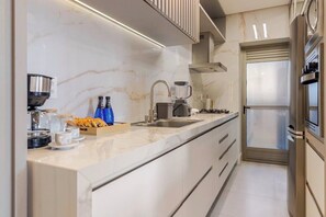 A modern kitchen with a marble countertop, a built-in stove, a sink, and a refrigerator. - Luxury 2BR • 2 Min Walk to Beach • Rooftop Pool • BBQ • 2 Parking (Florianópolis)