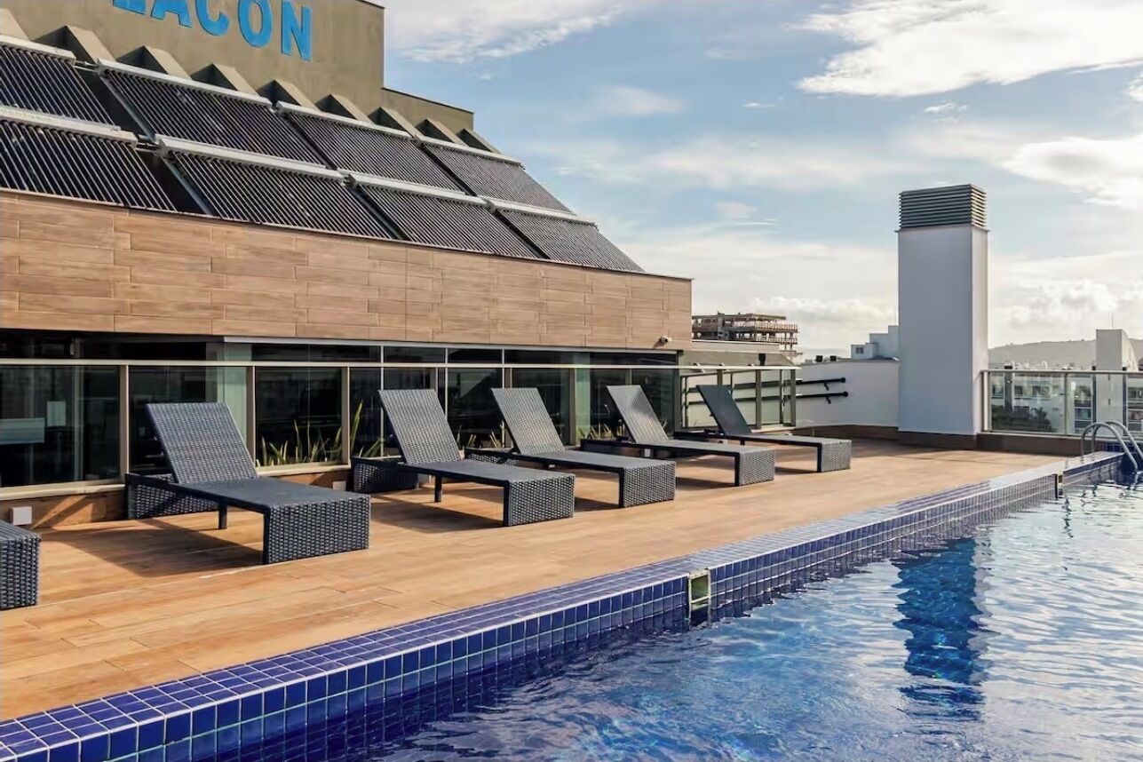 A rooftop pool area with lounge chairs, a swimming pool, and a building with solar panels.
