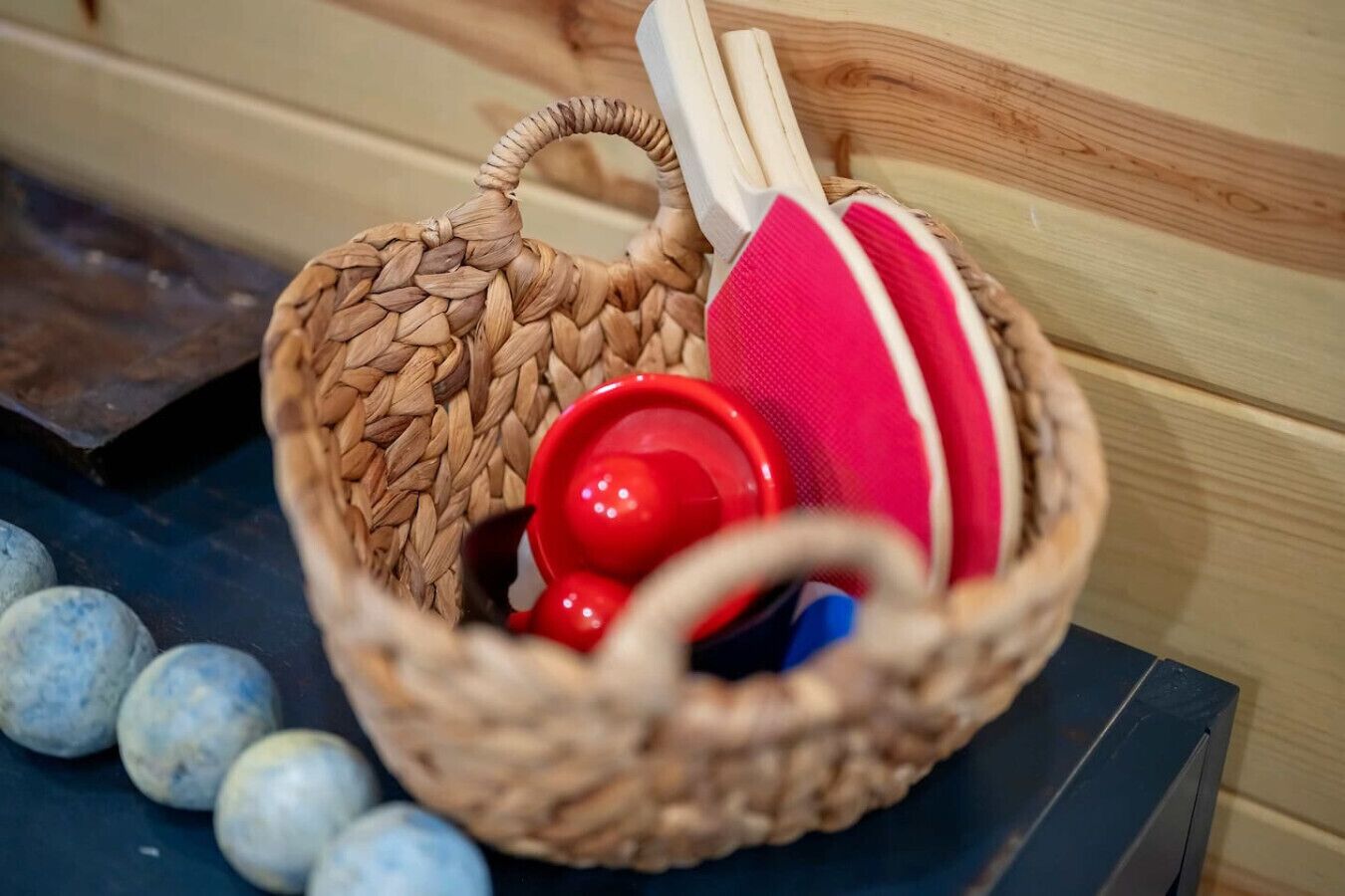 A woven basket containing a red object, a white object, and a pink object, placed on a dark surface with blue spherical objects nearby.