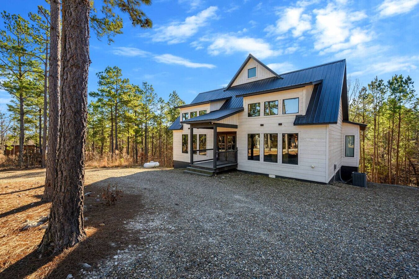 A modern two-story house with a covered porch, large windows, and a gravel driveway.