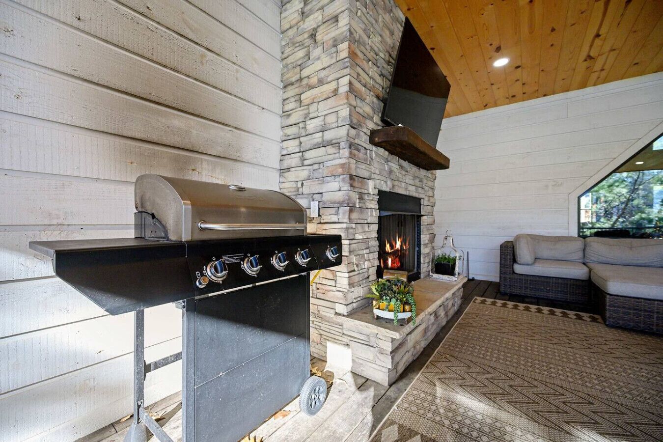Una chimenea de piedra con una parrilla, un sofá de mimbre y vistas al exterior.