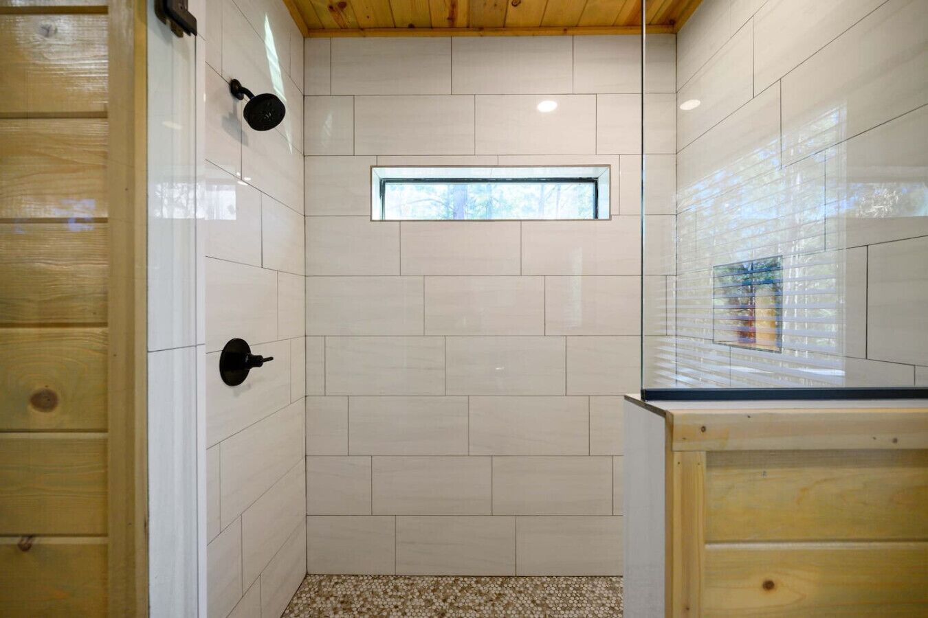 Una ducha con azulejos blancos, techo de madera y una pequeña ventana.