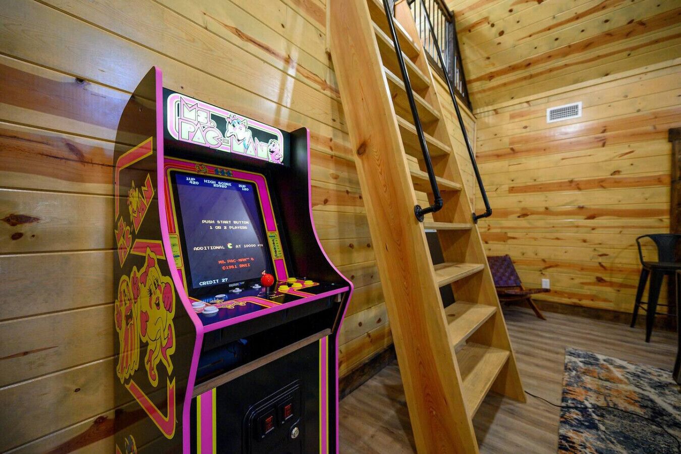 Une borne d’arcade avec un jeu de griffe, installée dans une cabane en bois avec un escalier.