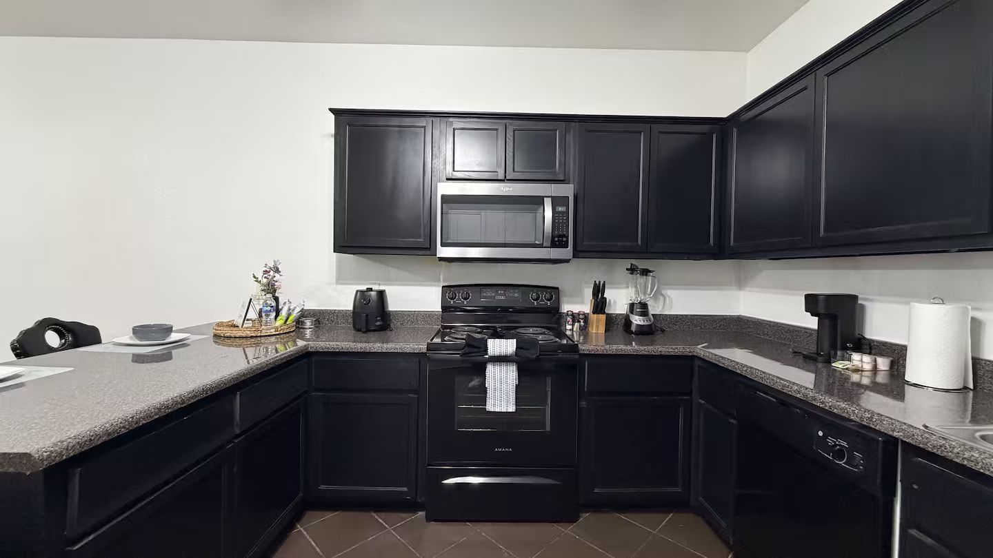 Una cocina con armarios negros, un microondas, una estufa y un lavavajillas.