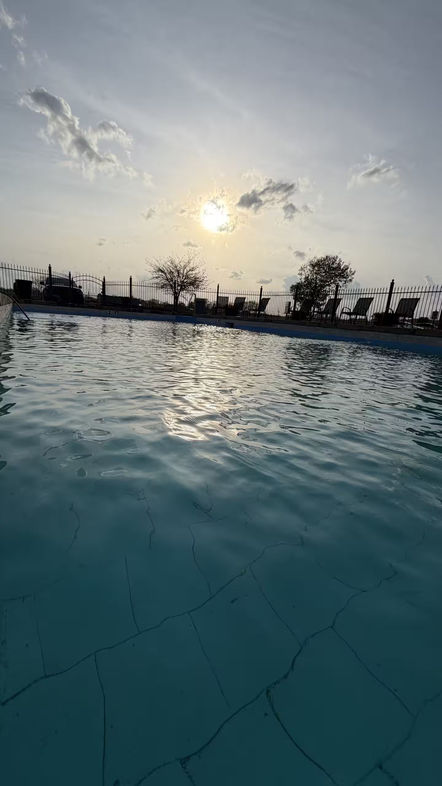 Una piscina con una cerca y sillas de descanso al fondo.